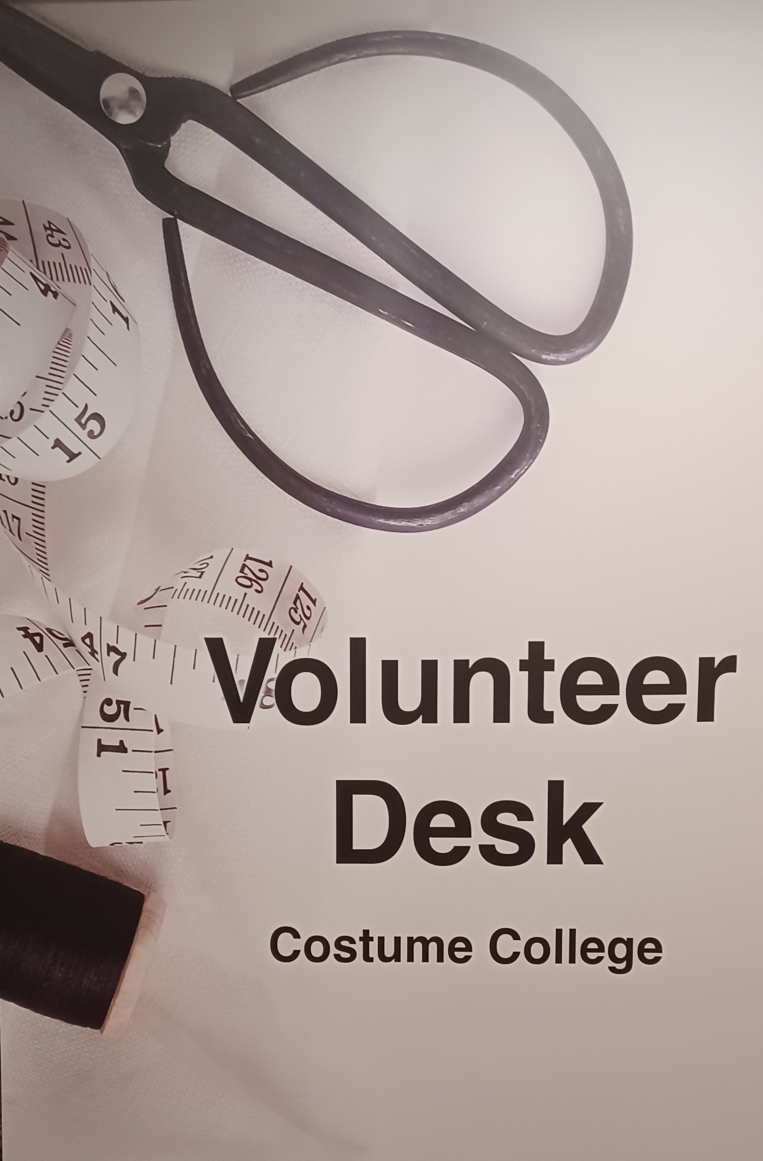 Metal sewing scissors at the top of the image with an unrolled white tape measure and spool of black tread below To the right is the text: Volunteer Desk Costume College. 